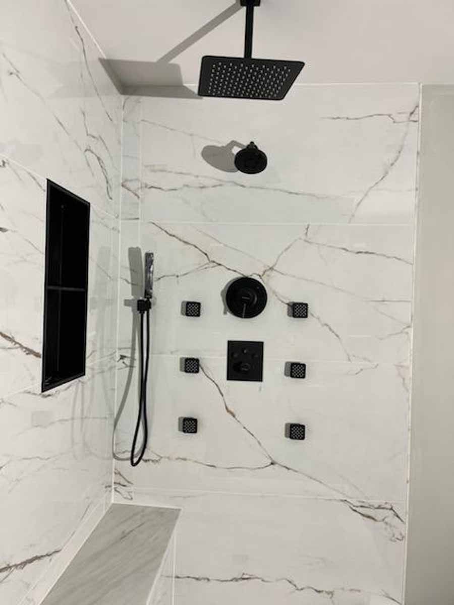 Modern shower with marble-like tile, black fixtures, including a rain shower head, handheld shower, and body jets.