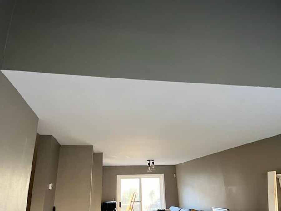 Interior view of a room with a white ceiling and taupe-colored walls, partially obstructed by a dark gray beam.