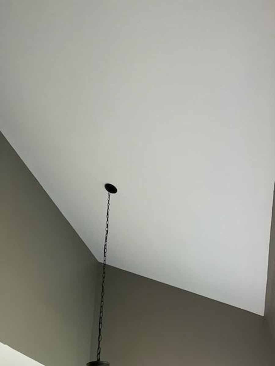 Black pendant light chain and fixture hanging from a white sloped ceiling, against grey walls.