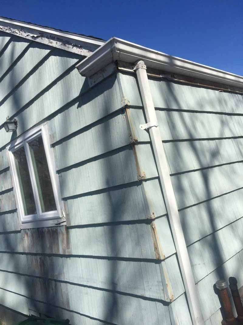Light blue siding on a house with white gutters and downspout, and a window.