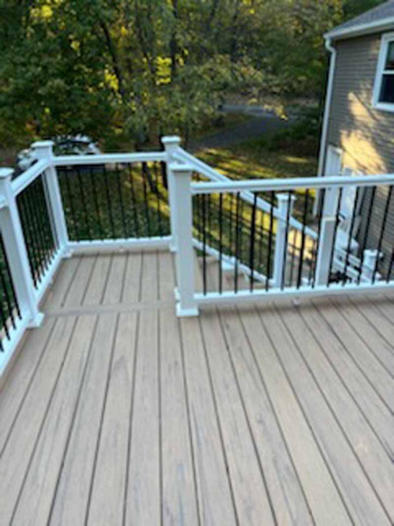 Wooden deck with white railings and black spindles, overlooking a yard and house.