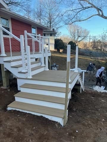 Newly constructed outdoor deck with white railing, steps, and composite decking. Workers are present.