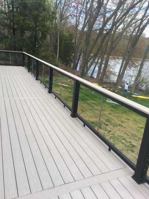 Wooden deck with black railings and glass panels overlooking a lake.