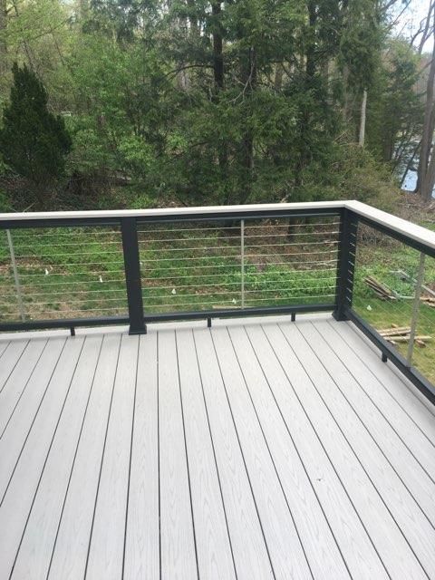 Deck with gray composite decking and black metal railing with cable infill, overlooking a grassy yard and trees.