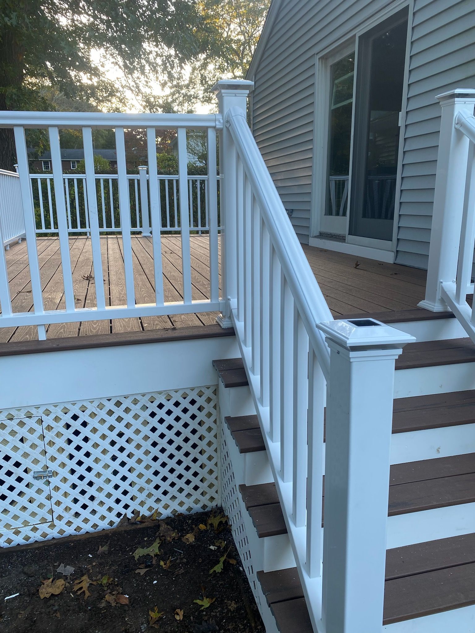 White deck with stairs, composite decking, and lattice skirting against a house with sliding glass doors.