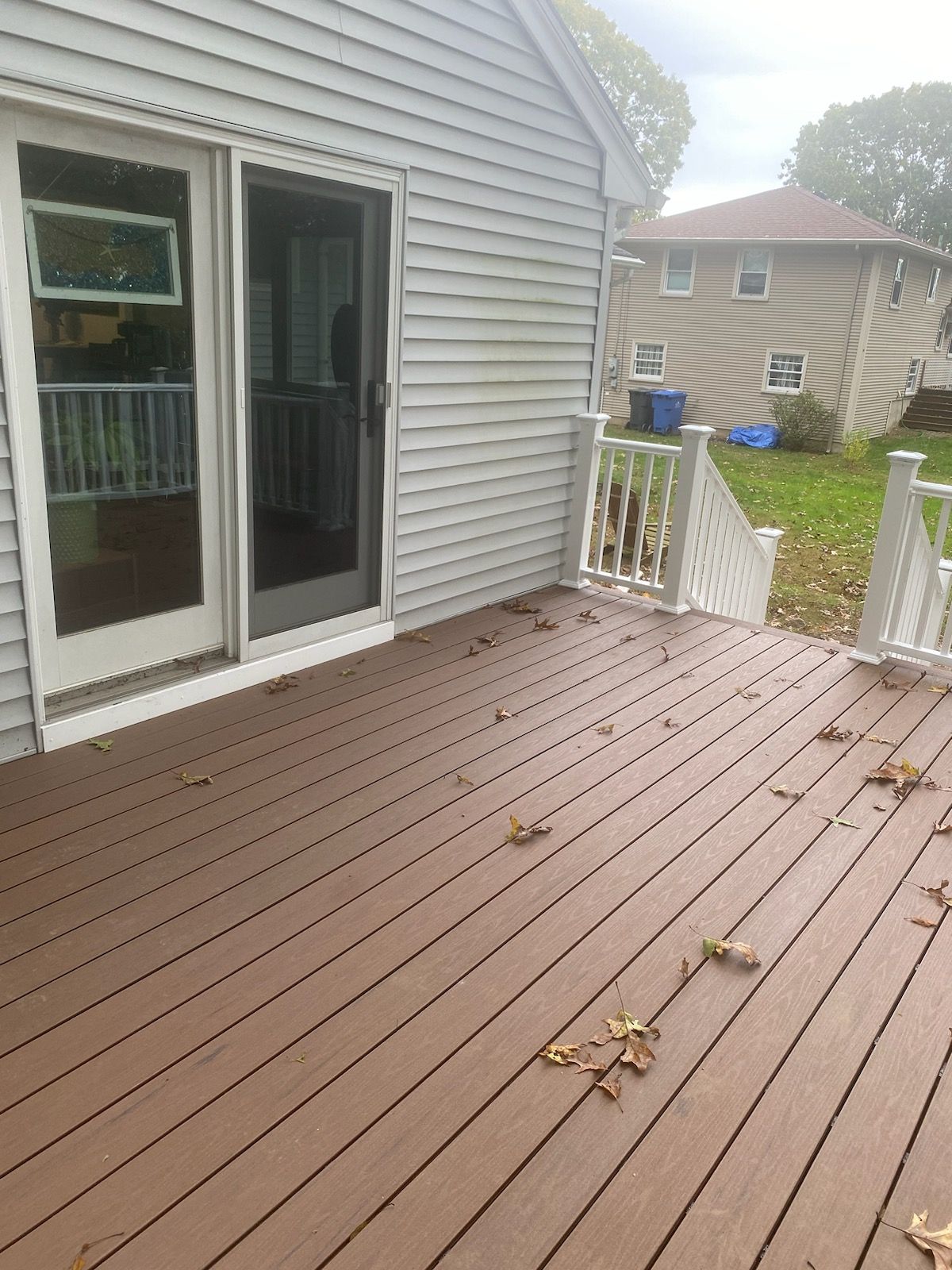 Deck attached to a house with sliding glass door. Composite deck boards, white railing, and a lawn.