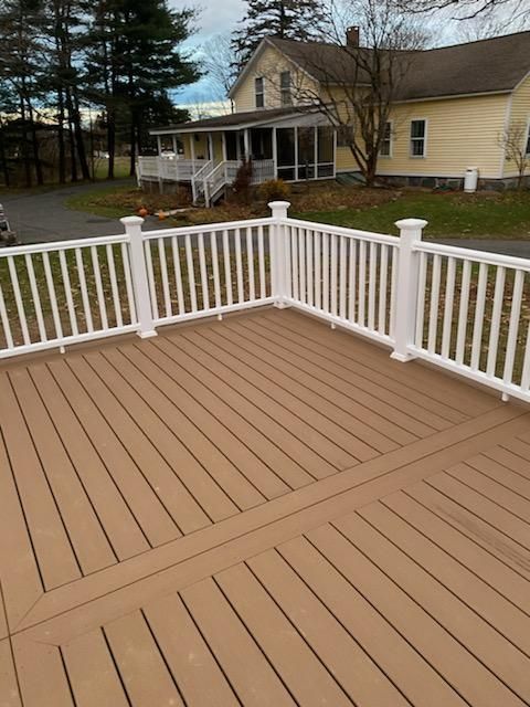 Brown composite deck with white railing in front of a yellow house.