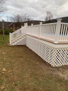 White lattice-skirted deck with stairs and railing surrounding a pool. Overcast day, outdoors on grass.