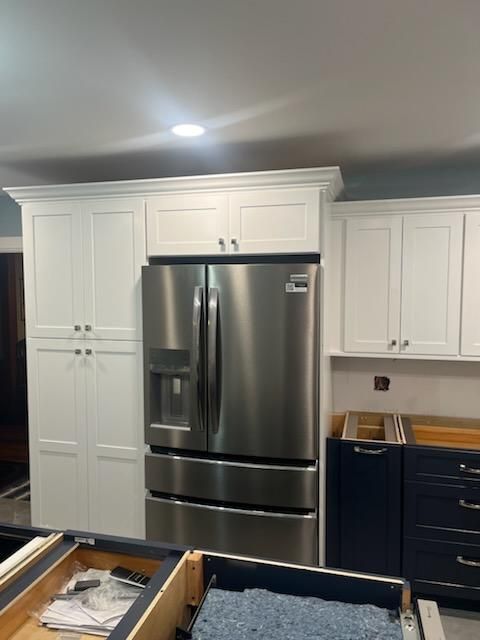 White kitchen cabinets surround a stainless steel refrigerator.  A small, dark blue cabinet with drawers is visible.