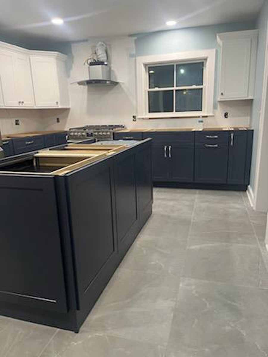 Modern kitchen renovation with dark blue cabinets, white upper cabinets, and gray tile flooring.