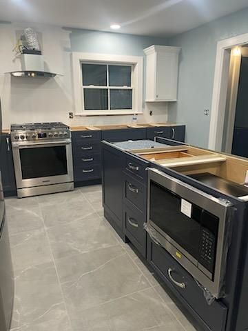 Kitchen remodel in progress; dark blue cabinets, stainless steel appliances, light gray tile floor, white walls.