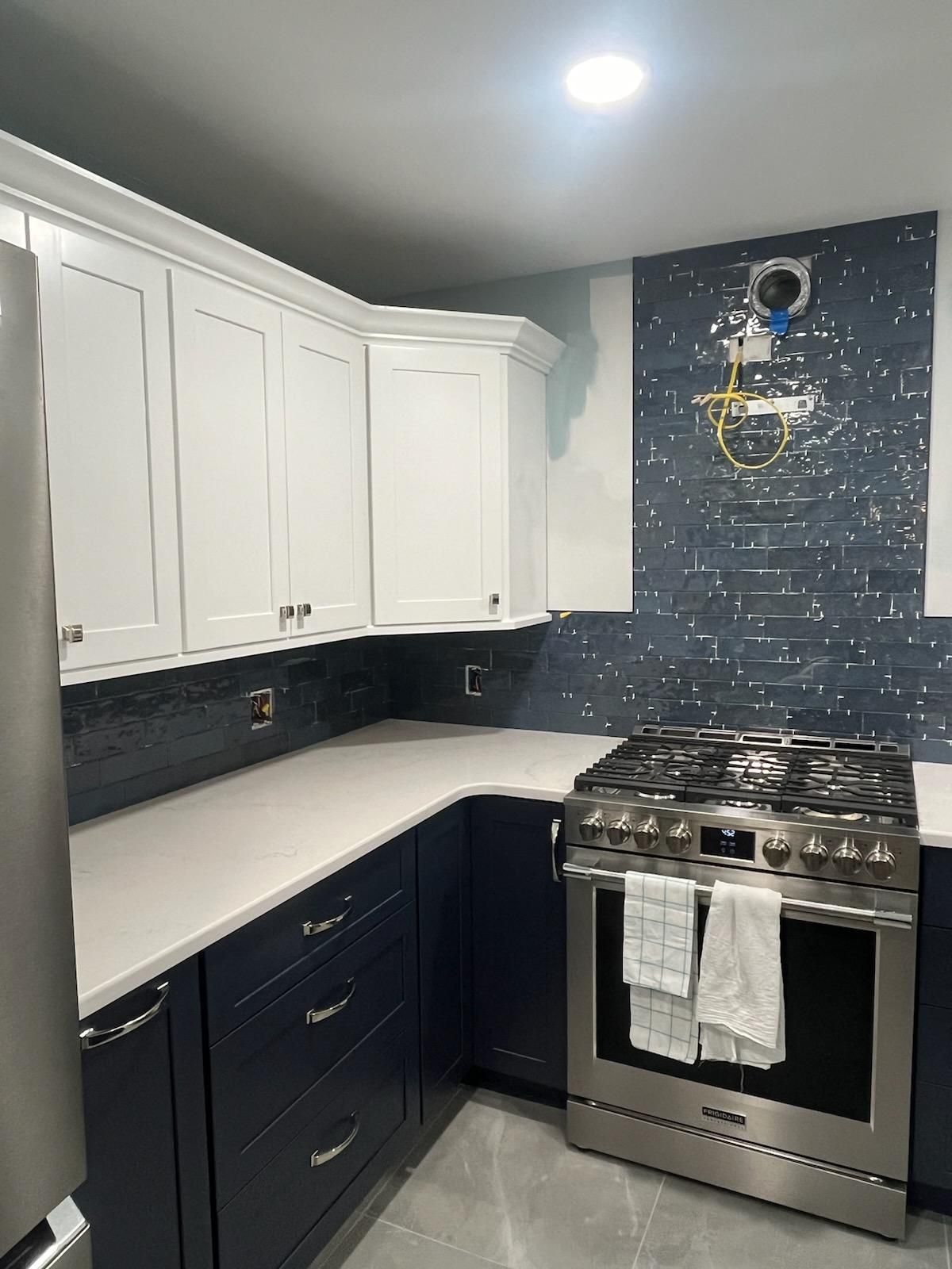 Kitchen remodel with white and navy cabinets, white countertops, and navy backsplash. Stainless steel range.