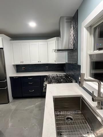 Modern kitchen with white upper cabinets, dark blue lower cabinets, stainless steel appliances, and a quartz countertop.