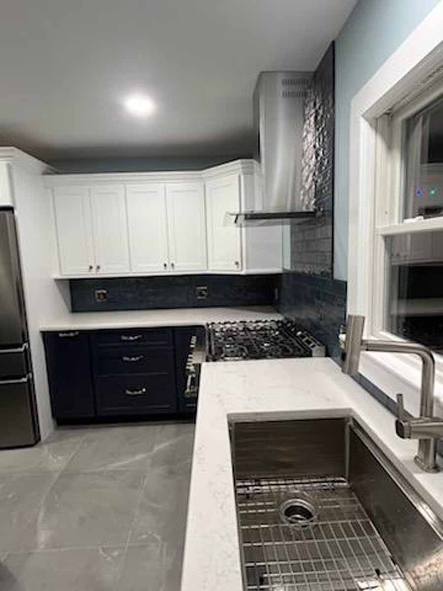 Modern kitchen with white and navy blue cabinets, stainless steel appliances, and a tiled backsplash.