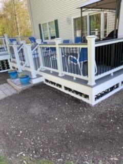 A multi-level deck with white and black railings, surrounded by gray gravel and a partially visible house.