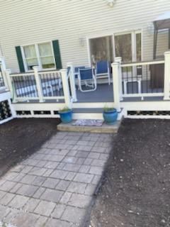 Paver walkway leading to a deck with blue chairs and potted plants.