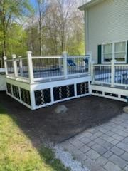 White deck with black lattice panels next to a house with a green lawn.