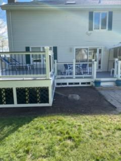 Back of a two-story white house with a multi-level wooden deck. The deck has a railing and connects to a sliding glass door.