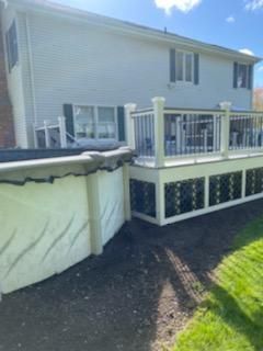 Backyard with above-ground pool and deck. The house is light-colored. The yard has grass and dirt. Sunny day.