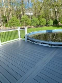 Gray deck surrounding a covered above-ground pool; black railing and trees in background.