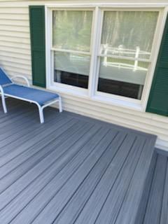 Deck with blue-gray composite boards, green shutters, white windows, and a blue lounge chair.