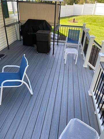 Gray composite deck with blue chairs, grill, and black railing. Backyard setting with white fence.
