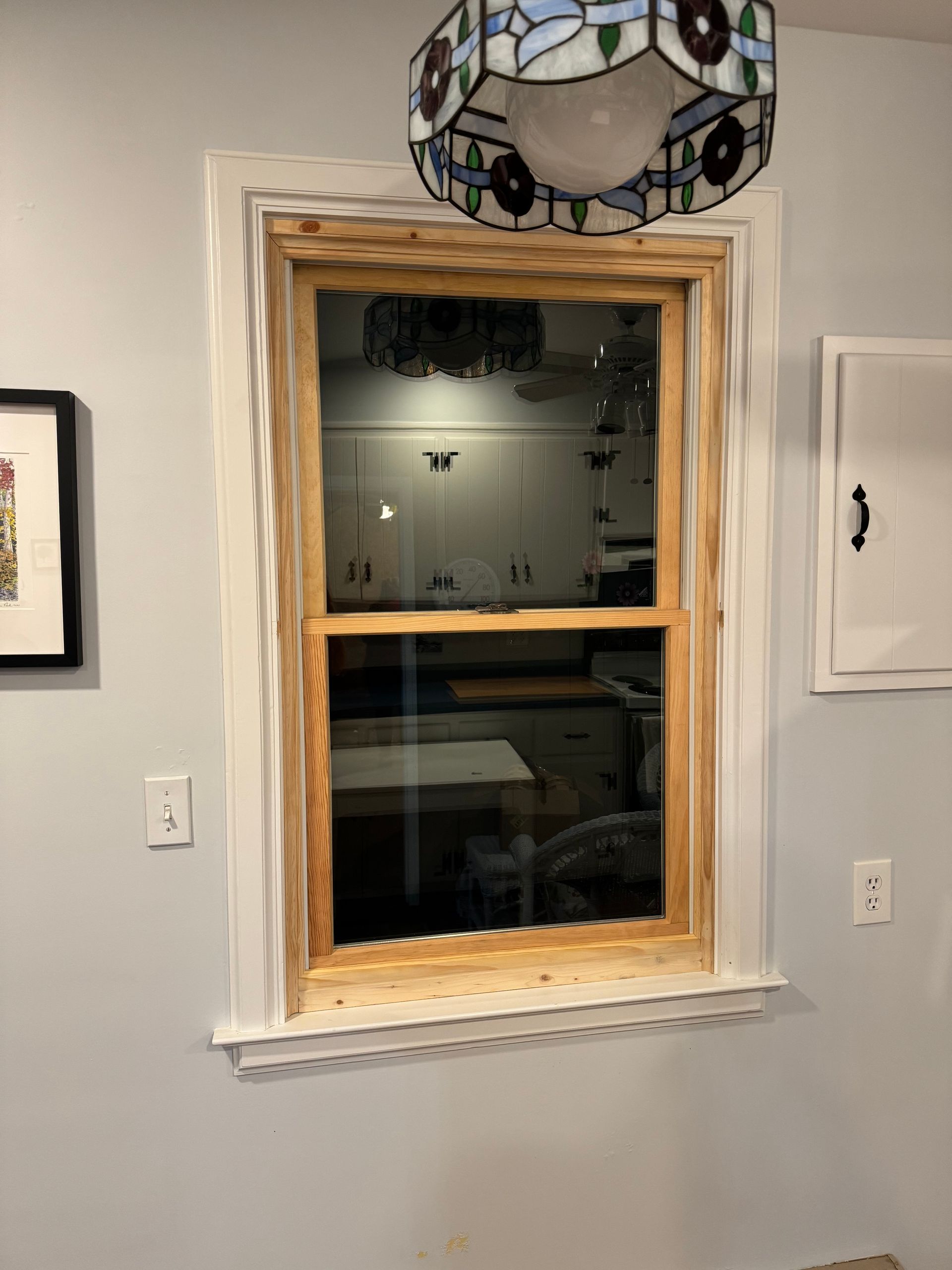 A newly installed window with white trim, stained wood frame, and a hanging stained-glass lamp.