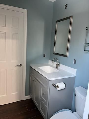 Bathroom with gray vanity, white countertop, silver faucet and mirror, blue walls, white door, and toilet.
