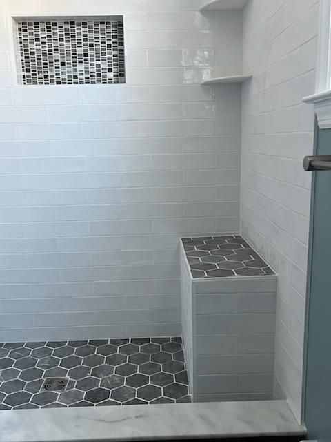 White tiled shower with a gray tiled bench, niche, and floor.