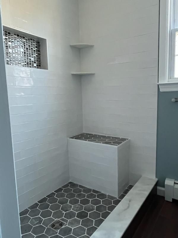 A modern, tiled shower with a built-in bench. Hexagonal floor tiles, white walls, two corner shelves.