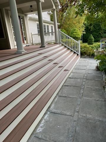 Wooden porch steps with a white railing and stone walkway.