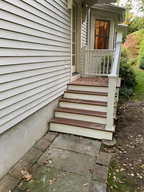 Exterior view of steps leading to a doorway, with a white railing and siding.