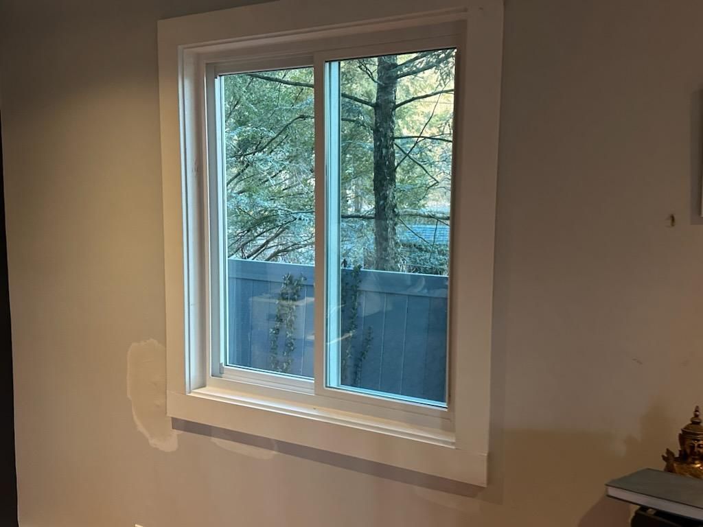 White-framed window in a room, looking out to a blurred green tree and blue fence.