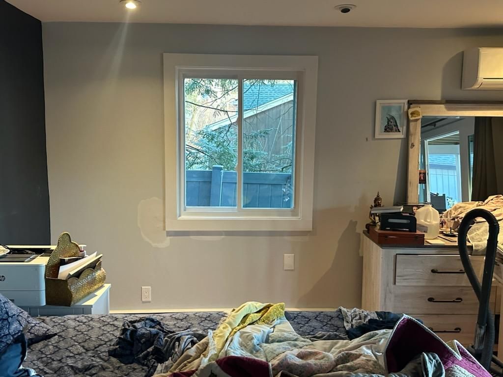 Bedroom with a window, cluttered bed, dresser, and wall-mounted air conditioner.