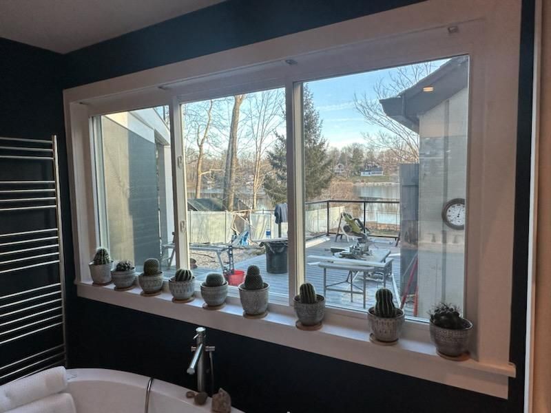 Bathroom window overlooking a patio and a lake, with cacti on the windowsill.