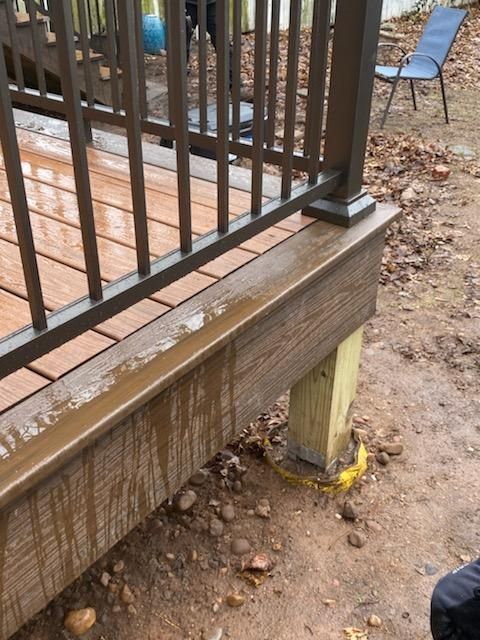 Deck with brown composite boards, dark railing, and a wooden post on muddy ground.