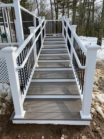 Stairs with white posts and black railings. Wooden steps lead up from snow-covered ground to a deck.
