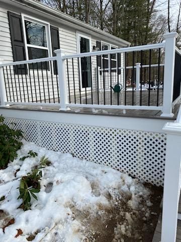 Deck with white railing and black spindles, lattice skirting, and snow-covered ground.