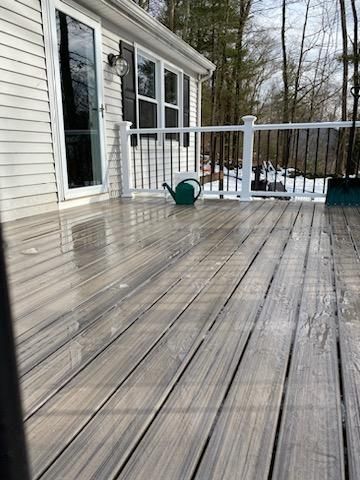 Wet composite deck in front of a house, with a watering can and a snow-covered background.