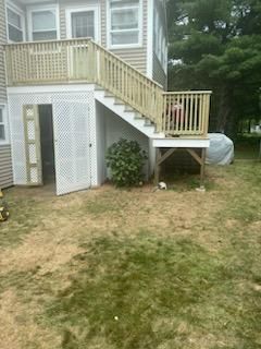 Wooden deck and stairs with latticework and storage beneath, set in a yard with dry grass.