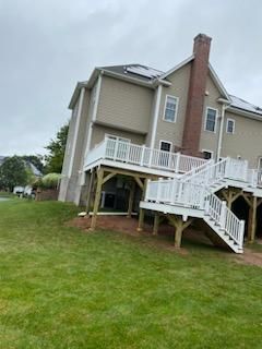 A two-story house with a wooden deck and stairs, set on a green grassy slope.
