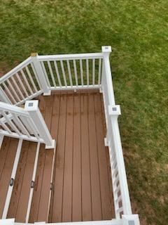 Brown deck with white railing and stairs against a green lawn.
