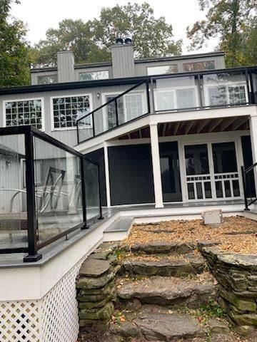Gray house with glass-paneled deck railing and stone steps leading up to it.