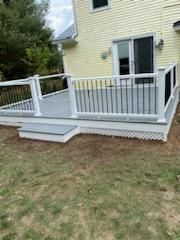 Newly constructed gray deck with white railing, black spindles, and a yellow house in the background.