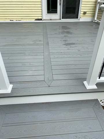 Gray composite deck with a darker central design, leading to a doorway. White railing on the right.