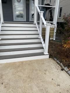 Gray and white steps leading up to a house entrance, with white railing and a concrete walkway.