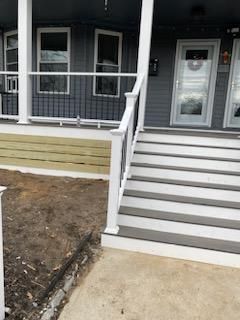 Gray and white house exterior with stairs and porch; a dirt area is in front.