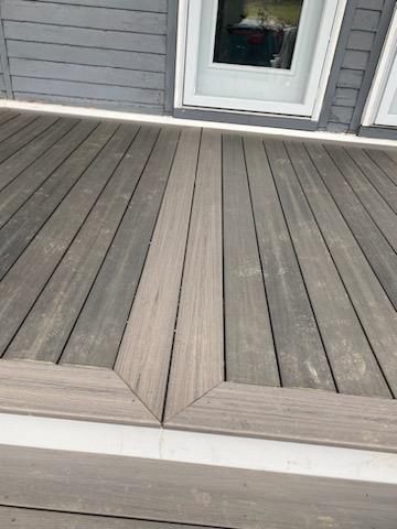 Wooden deck with angled border in front of a gray house.