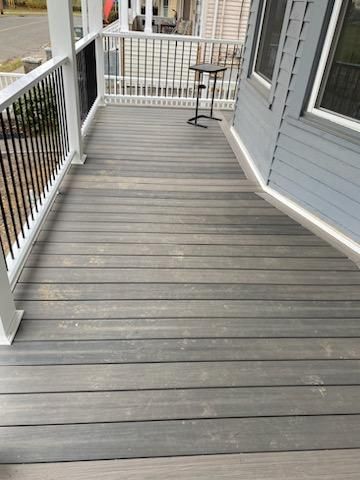 Gray wooden porch with a white railing and a small table.