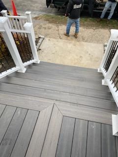 Gray composite deck with stairs and white railing. Two people standing on the concrete pathway.